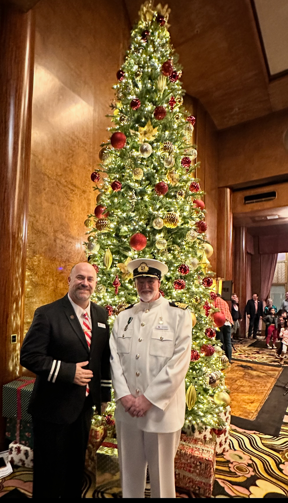 two men in uniform standing in front of a christmas tree